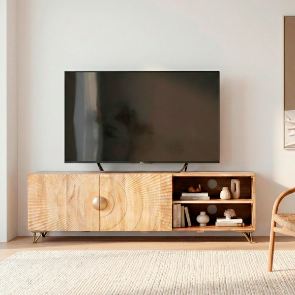 Mueble para TV de madera maciza con puertas talladas y patas metálicas Este mueble bajo de TV combina diseño artesanal y funcionalidad moderna. Fabricado en madera natural con puertas decoradas con tallado circular, ofrece un estilo único ideal para salones contemporáneos o rústicos. Cuenta con compartimentos abiertos con orificios pasacables, perfectos para equipos electrónicos. Sus patas metálicas elevadas aportan estabilidad y un toque industrial.